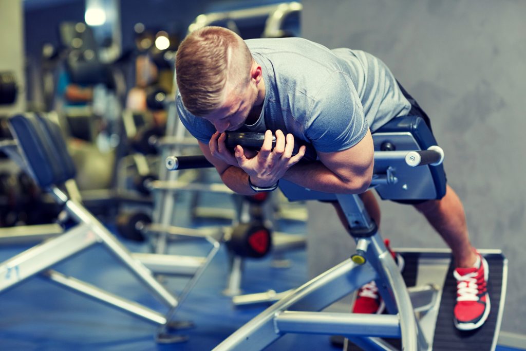 young man flexing back muscles on bench in gym
