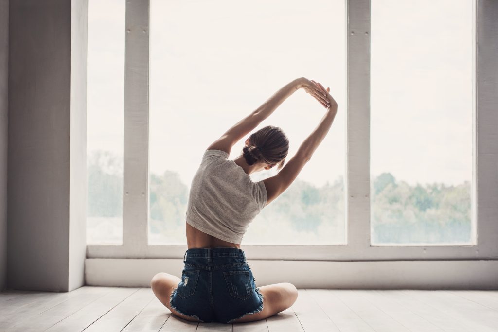 Woman doing yoga and stretching at home in front of window.